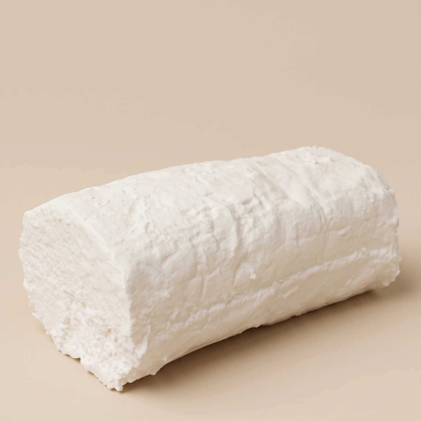 Queso fresco de cabra artesanal sobre fondo beige.